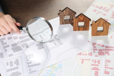 House hunting. Woman with maps, magnifying glass and house figures at wooden table, closeup