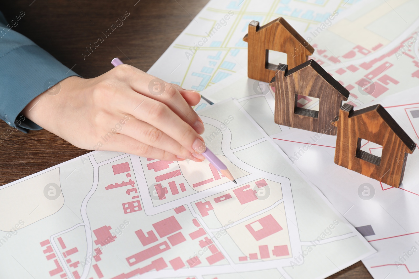 Photo of House hunting. Woman with maps and house figures at wooden table, closeup