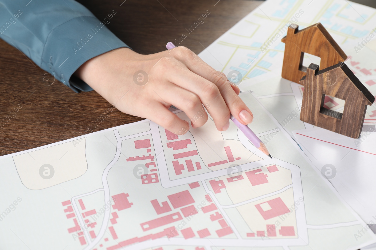 Photo of House hunting. Woman with maps and house figures at wooden table, closeup