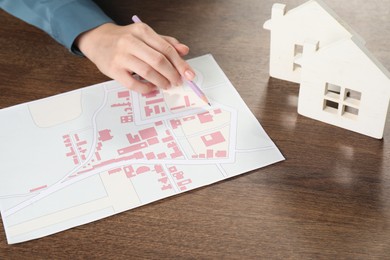 Photo of House hunting. Woman with map and house figures at wooden table, closeup