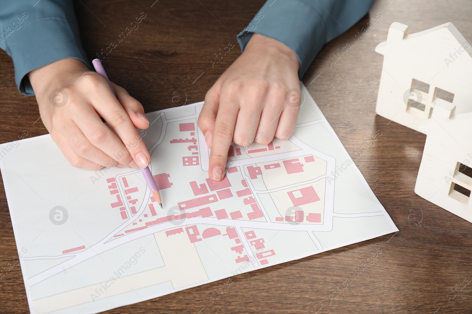 Photo of House hunting. Woman with map and house figures at wooden table, closeup