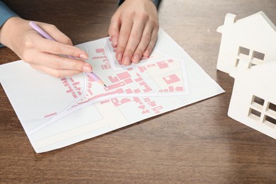 House hunting. Woman with map and house figures at wooden table, closeup