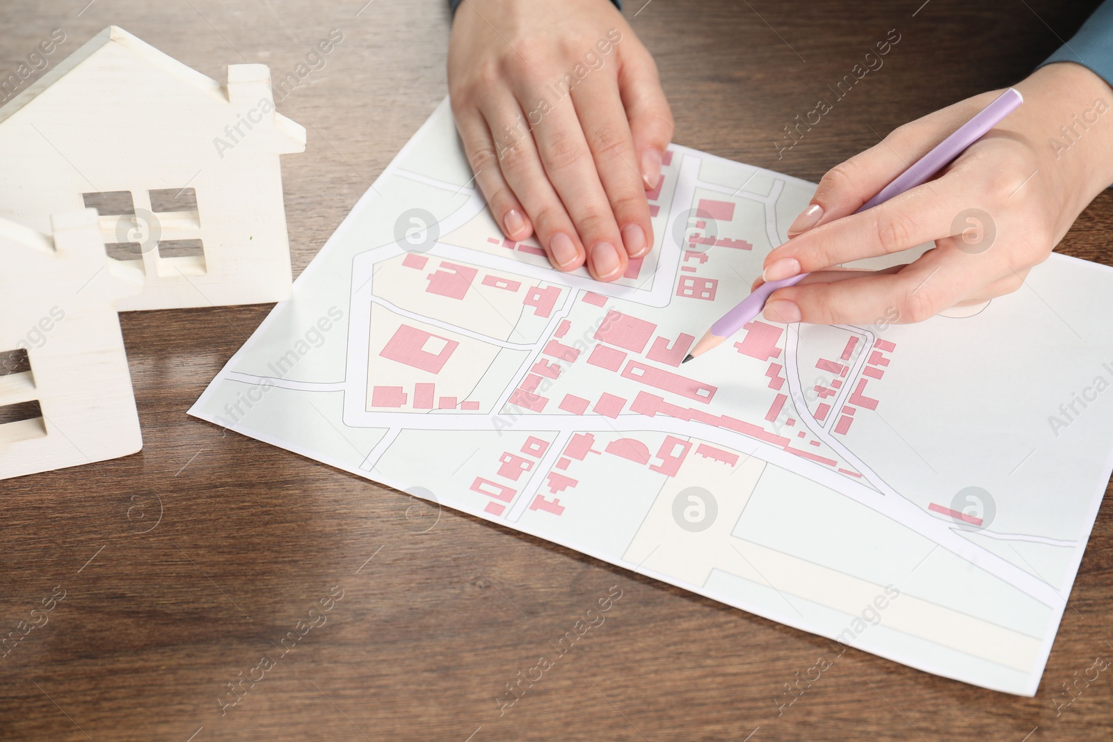 Photo of House hunting. Woman with map and house figures at wooden table, closeup