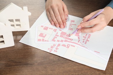 House hunting. Woman with map and house figures at wooden table, closeup