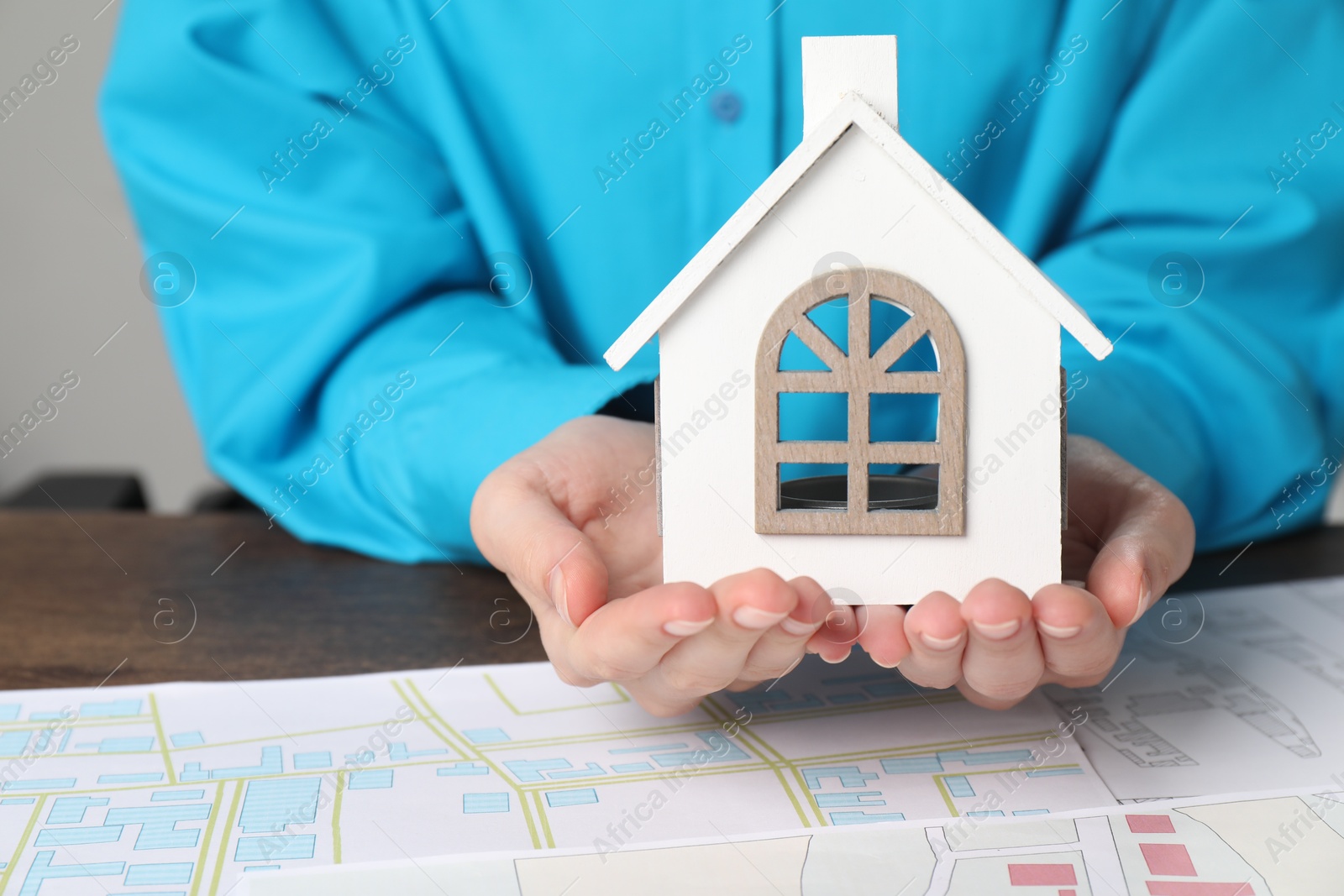 Photo of House hunting. Woman with maps and house figure at wooden table, closeup