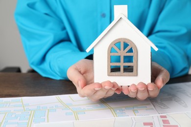 House hunting. Woman with maps and house figure at wooden table, closeup