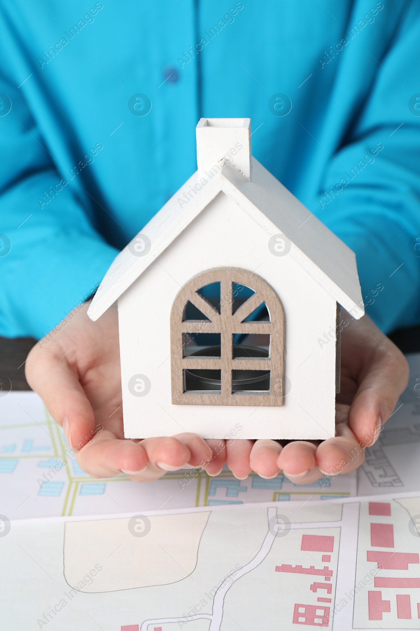 Photo of House hunting. Woman with maps and house figure at wooden table, closeup