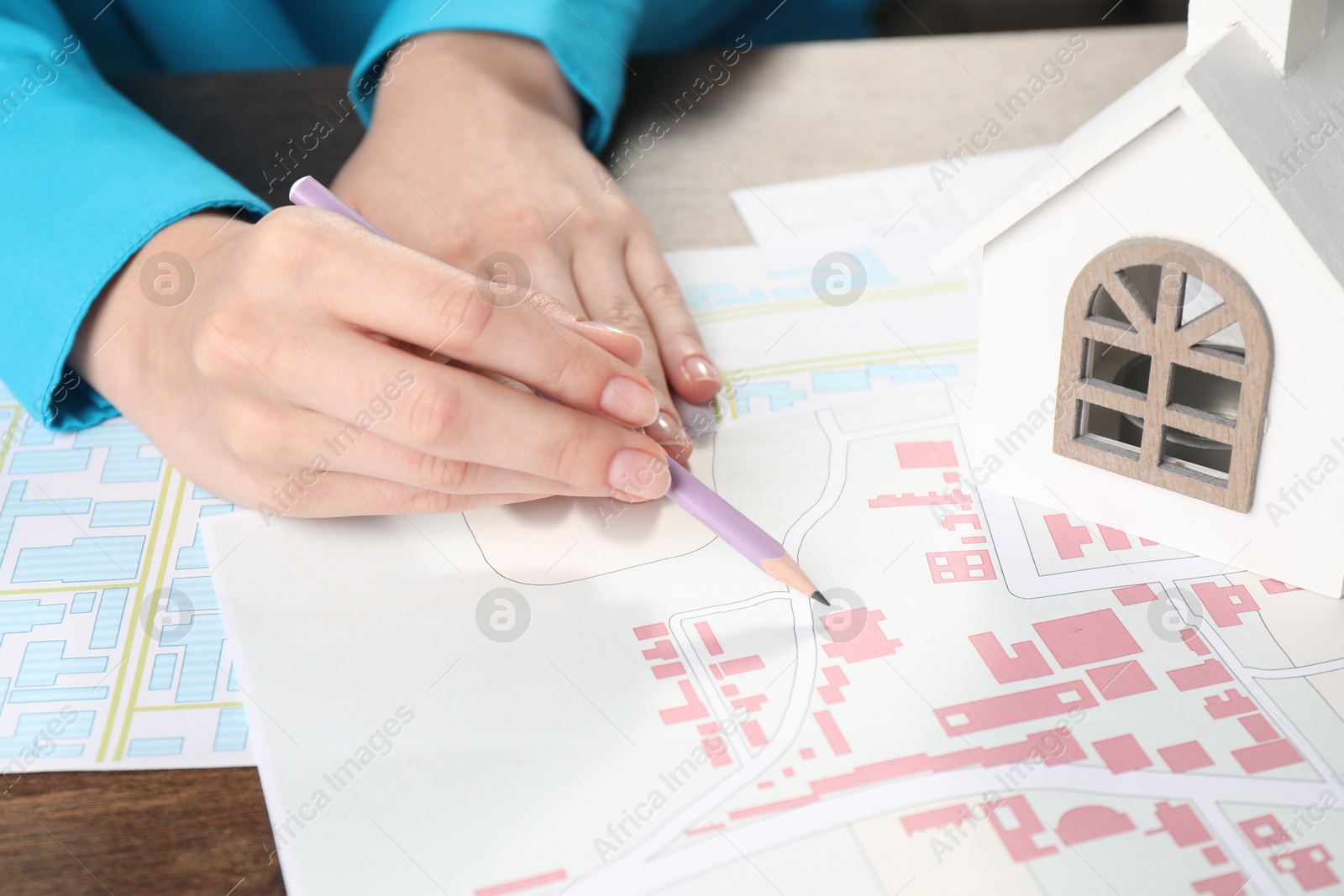 Photo of House hunting. Woman with maps and house figure at wooden table, closeup