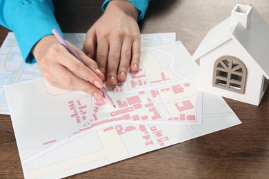 Photo of House hunting. Woman with maps and house figure at wooden table, closeup