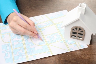 House hunting. Woman with map and house figure at wooden table, closeup