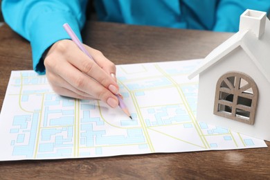 Photo of House hunting. Woman with map and house figure at wooden table, closeup