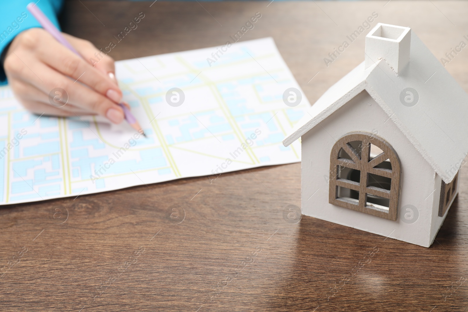 Photo of House hunting. Woman with map and house figure at wooden table, closeup