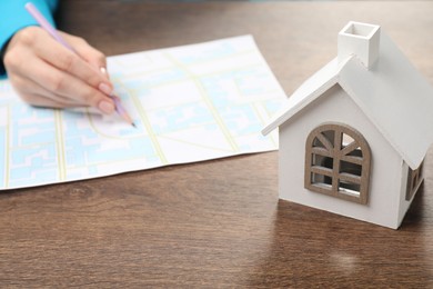 House hunting. Woman with map and house figure at wooden table, closeup