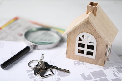 Photo of House hunting. Maps, magnifying glass, key and house figure on white marble table