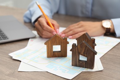 House hunting. Woman with laptop, papers and house figures at wooden table, closeup