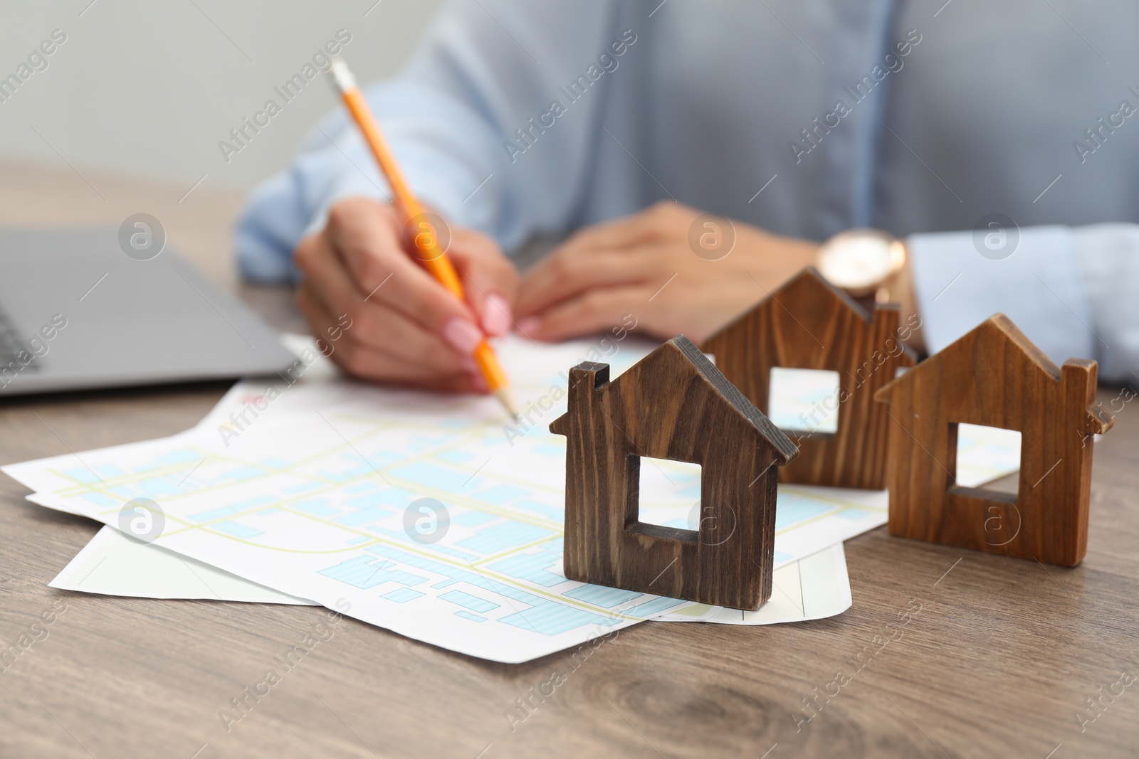 Photo of House hunting. Woman with laptop, papers and house figures at wooden table, closeup