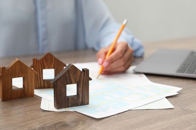 Photo of House hunting. Woman with laptop, papers and house figures at wooden table, closeup