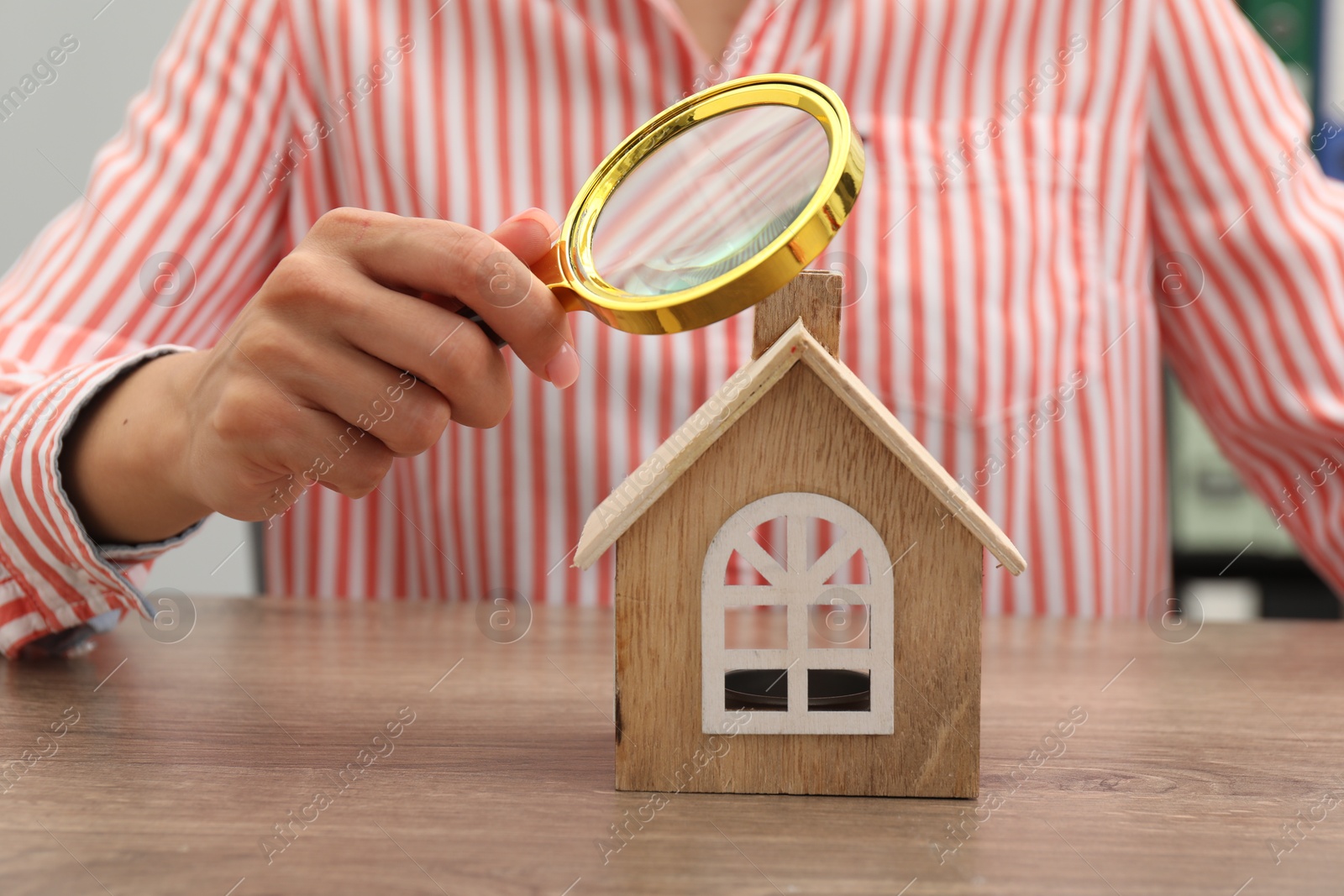 Photo of House hunting. Woman with magnifying glass and house figure at wooden table, closeup