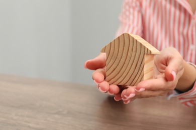 Photo of House hunting. Woman with house figure at wooden table, closeup. Space for text