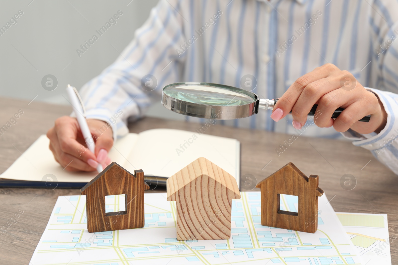 Photo of House hunting. Woman with papers, notebook and house figures at wooden table, closeup