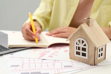 House hunting. Woman with laptop, papers and house figure at white table, closeup