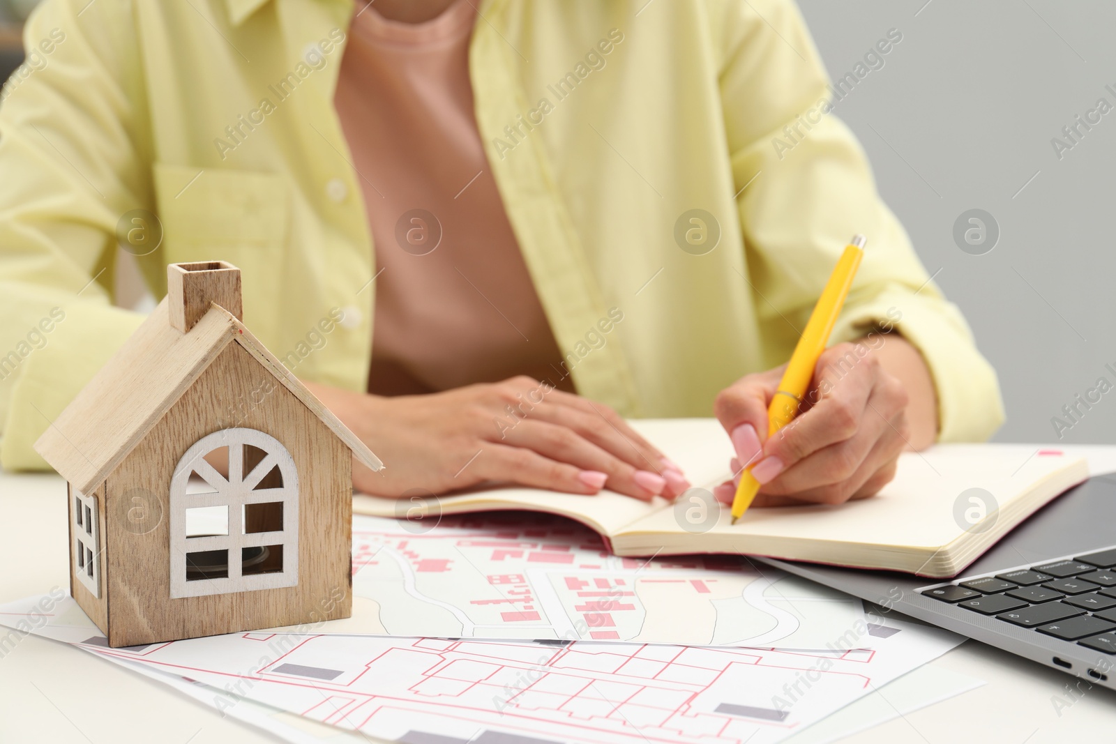 Photo of House hunting. Woman with laptop, papers and house figure at white table, closeup