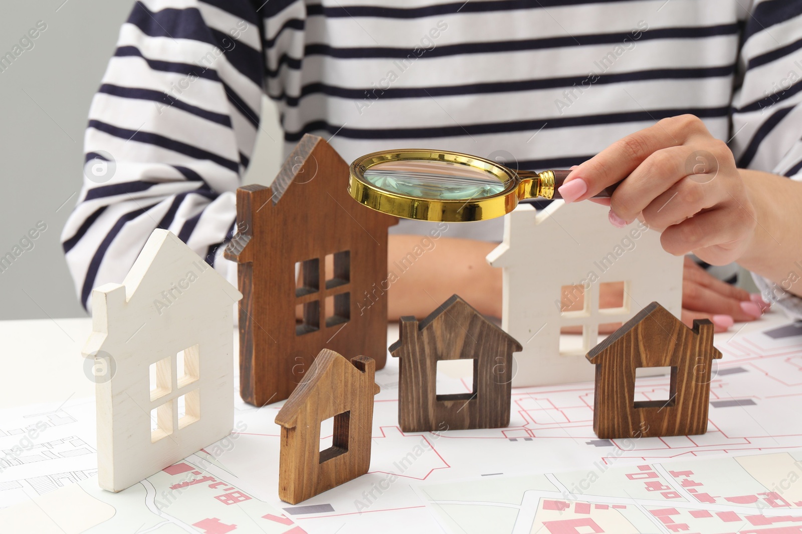 Photo of House hunting. Woman with maps, magnifying glass and house figures at white table, closeup