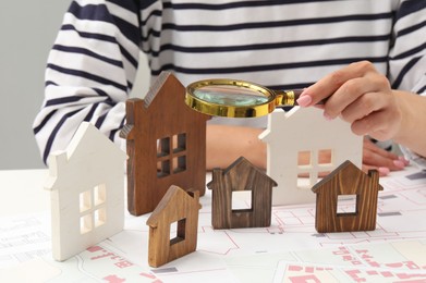 Photo of House hunting. Woman with maps, magnifying glass and house figures at white table, closeup