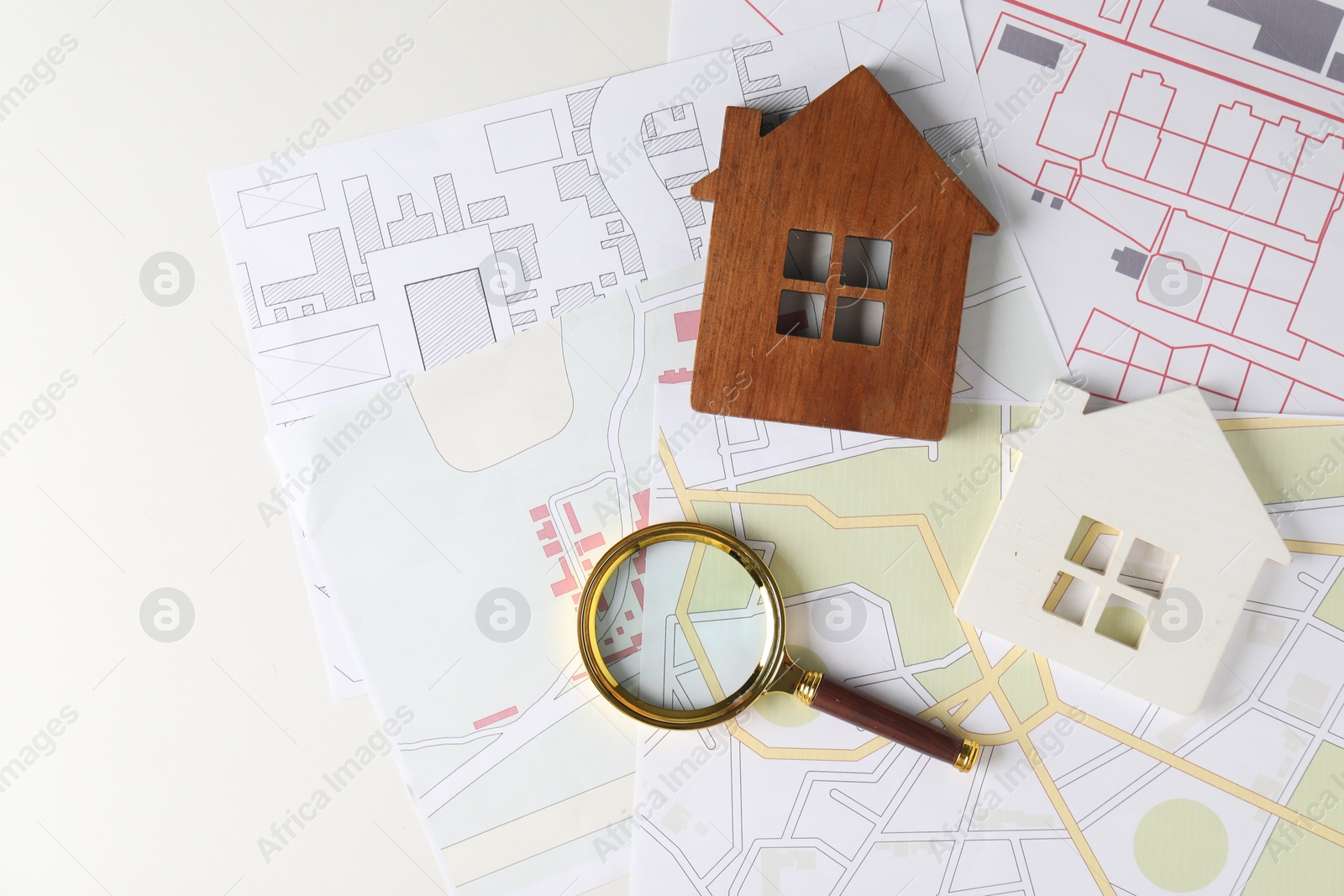 Photo of House hunting. Maps, magnifying glass and house figures on white table, flat lay. Space for text