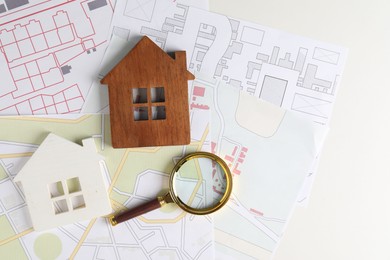 House hunting. Maps, magnifying glass and house figures on white table, flat lay. Space for text