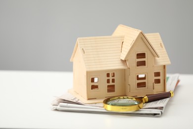 House hunting. Papers, magnifying glass and house figure on white table