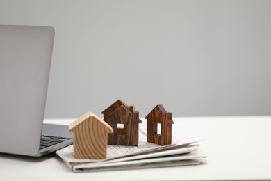 Photo of House hunting. Papers, laptop and house figures on white table, space for text