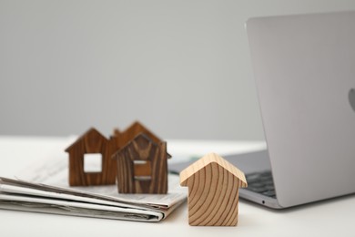 Photo of House hunting. Papers, laptop and house figures on white table