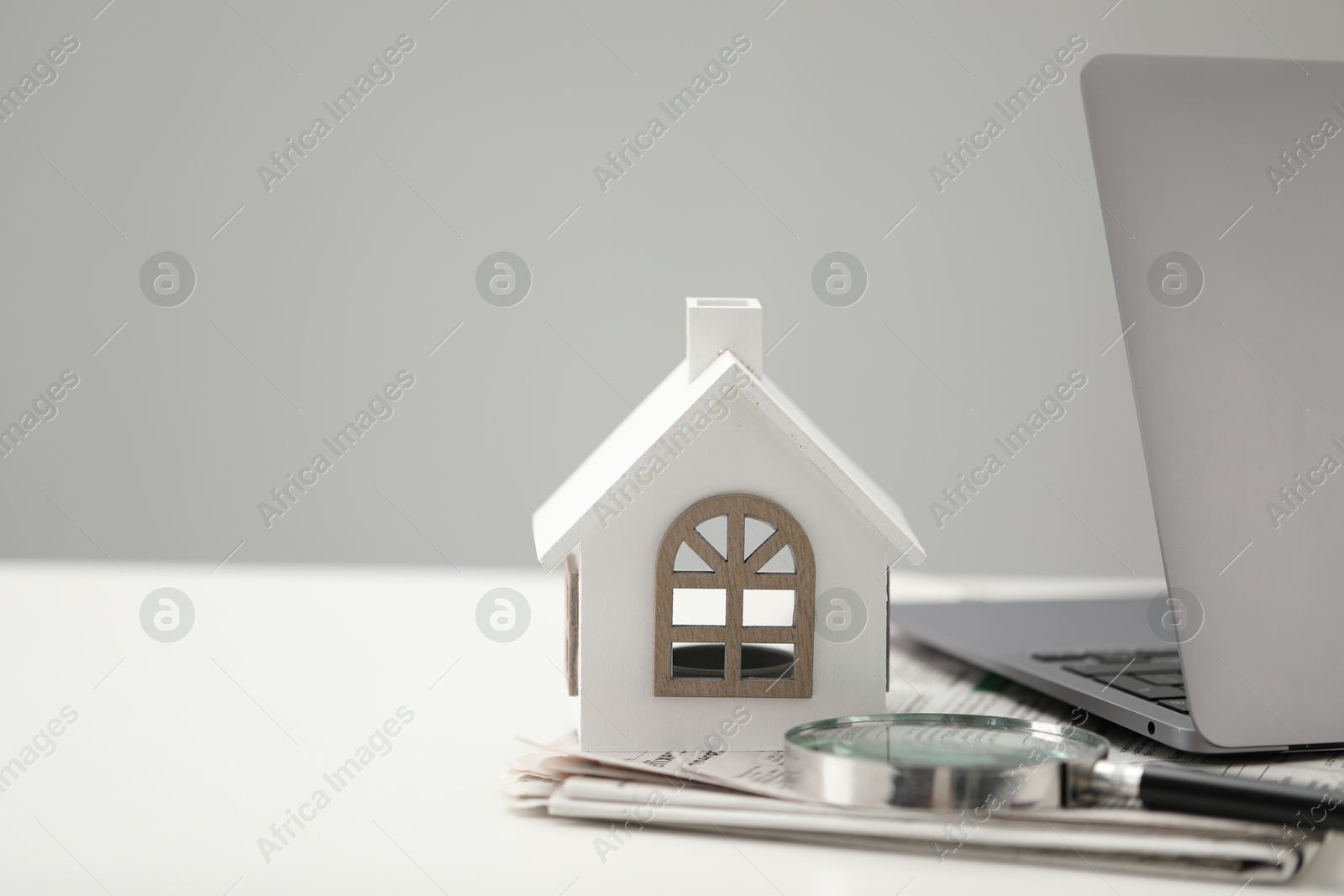 Photo of House hunting. Papers, magnifying glass, laptop and house figure on white table, space for text