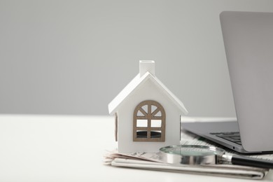 Photo of House hunting. Papers, magnifying glass, laptop and house figure on white table, space for text