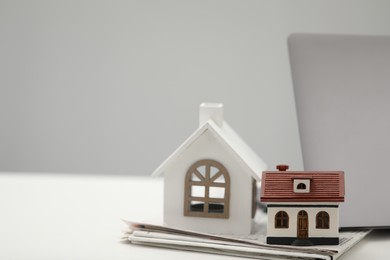 Photo of House hunting. Papers, laptop and house figures on white table, space for text