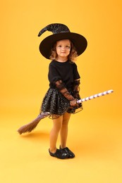 Photo of Cute girl with broom dressed like witch on yellow background. Halloween celebration