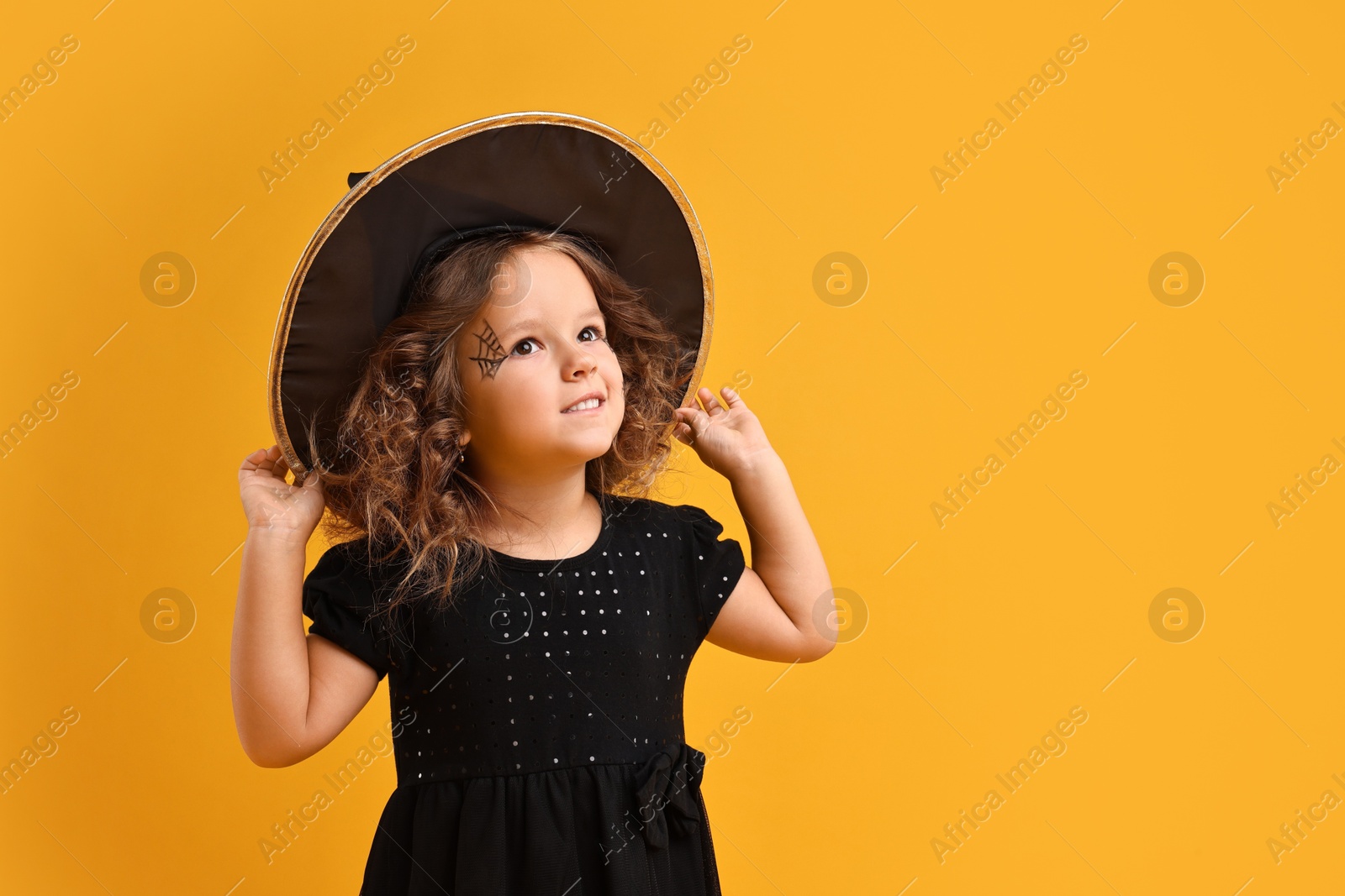 Photo of Cute girl dressed like witch on yellow background, space for text. Halloween celebration