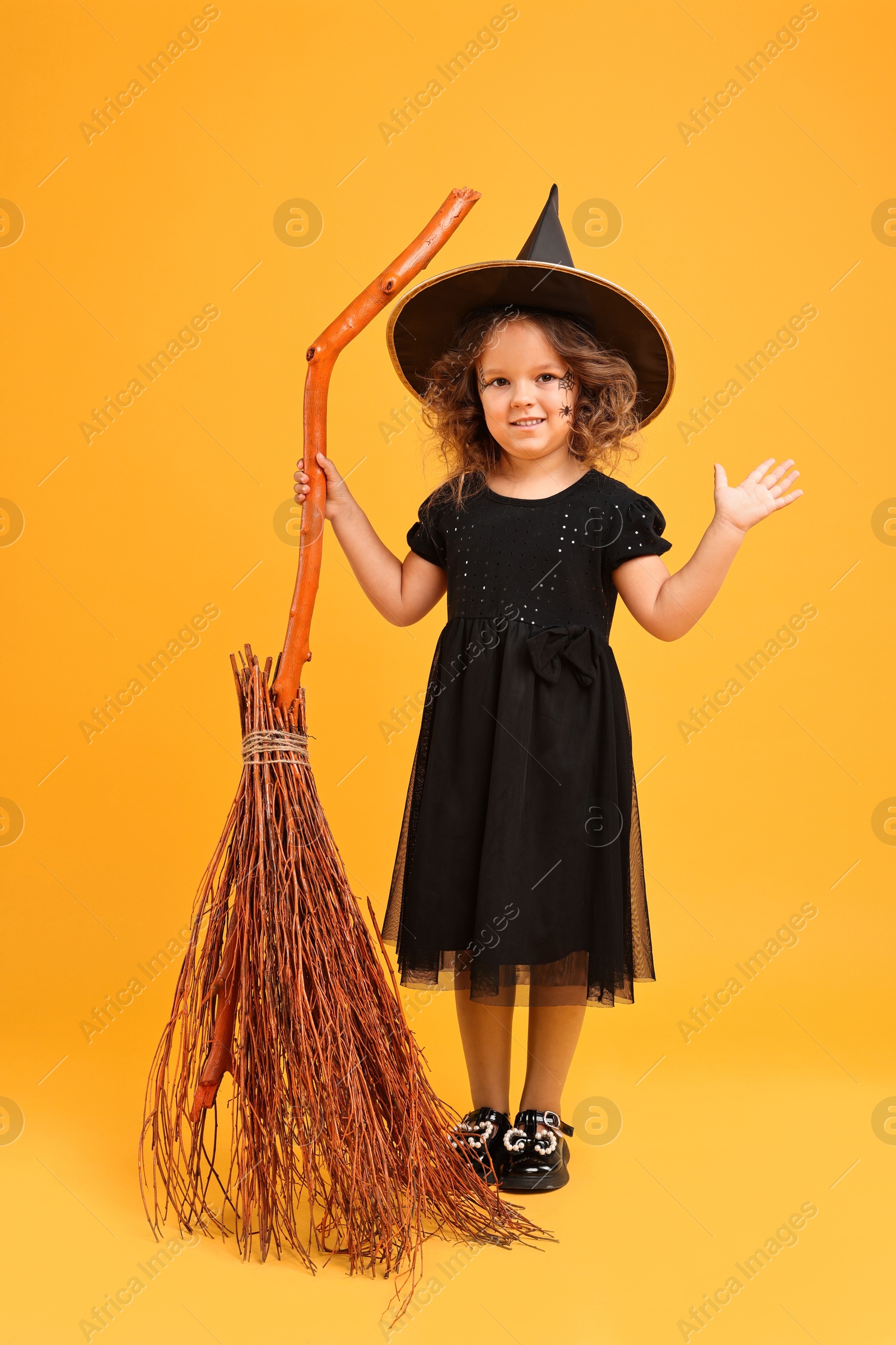 Photo of Funny girl with broom dressed like witch on yellow background. Halloween celebration