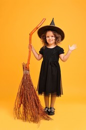 Photo of Funny girl with broom dressed like witch on yellow background. Halloween celebration