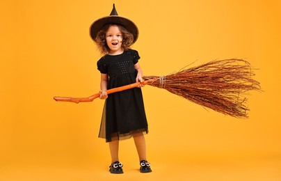 Photo of Funny girl with broom dressed like witch on yellow background. Halloween celebration