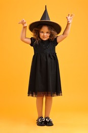 Cute girl dressed like witch on yellow background. Halloween costume