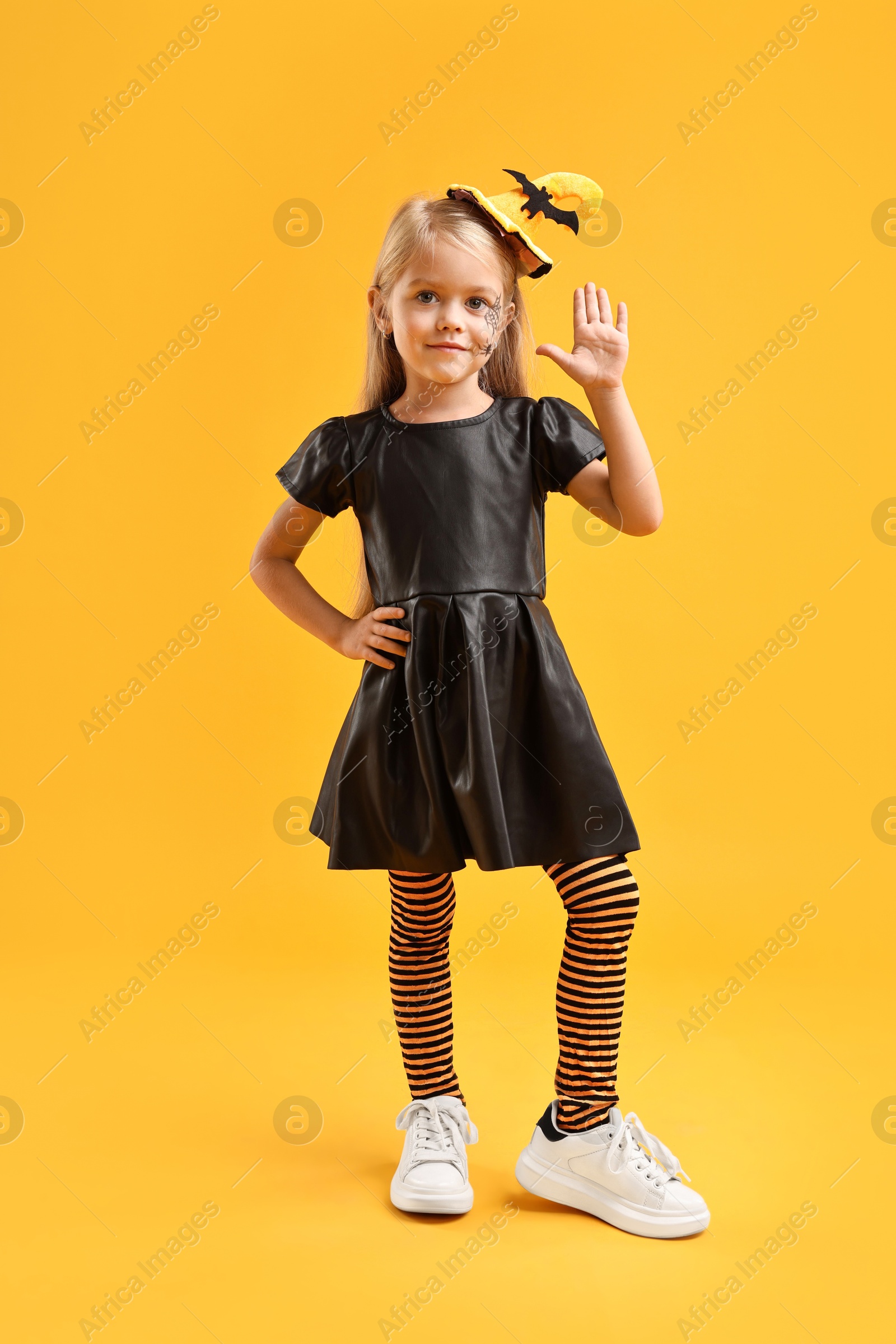 Photo of Cute girl dressed like witch on yellow background. Halloween celebration