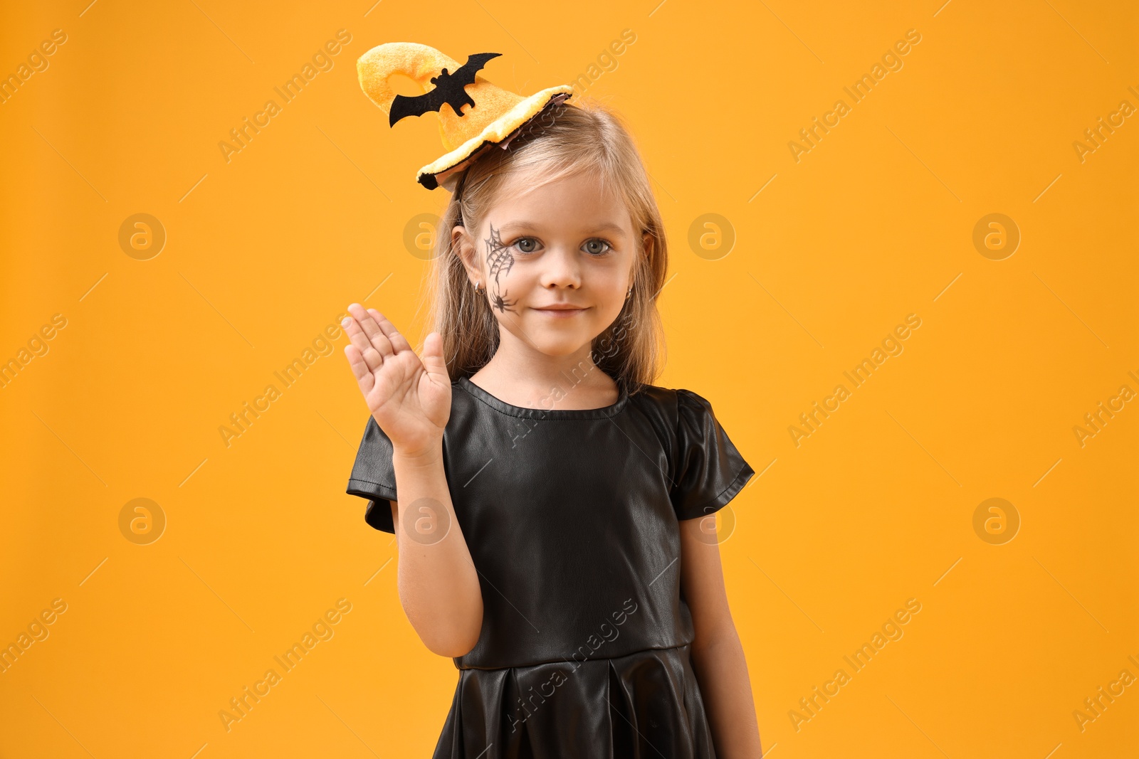 Photo of Cute girl dressed like witch on yellow background. Halloween celebration