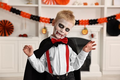 Photo of Funny boy dressed like vampire for Halloween celebration in room