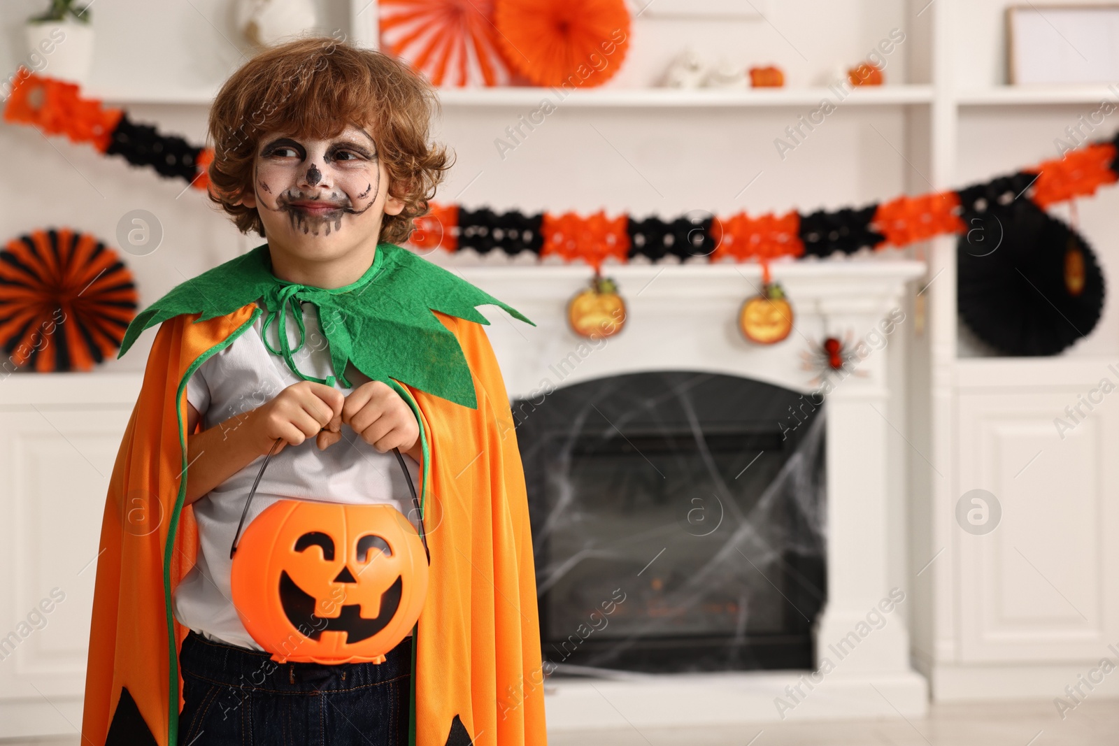 Photo of Funny boy with bucket dressed like pumpkin in room, space for text. Halloween celebration