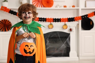 Funny boy with bucket dressed like pumpkin in room, space for text. Halloween celebration