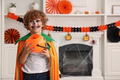 Photo of Funny boy with bucket dressed like pumpkin in room, space for text. Halloween celebration