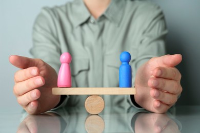 Gender equality concept. Woman with male and female figures on scales at grey table, closeup