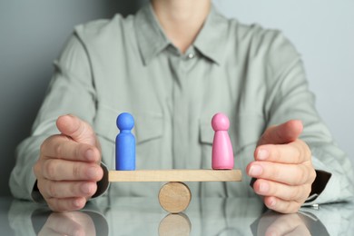 Gender equality concept. Woman with male and female figures on scales at grey table, closeup